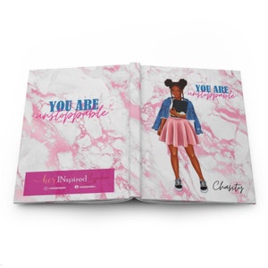 May include: Open journal with a pink marble design and the words "YOU ARE unstoppable" in blue and pink. The right side features an illustration of a person in a pink skirt and denim jacket. The name "Chasity" is written in cursive.