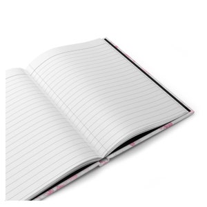 May include: Open notebook with lined pages. The notebook's cover features a pink floral pattern. The pages are white with gray lines, and the binding is black. The notebook is open, displaying the interior pages.
