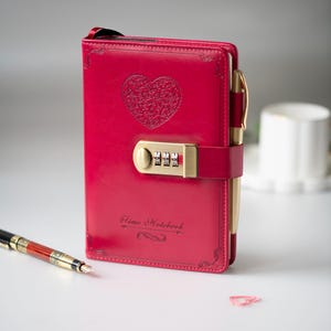 Op de afbeelding: Rood leren notitieboek met een hartvormig ontwerp en een combinatieslot. Het notitieboek heeft een penhouder en een gouden pen. De tekst "Time Notebook" staat op de kaft.