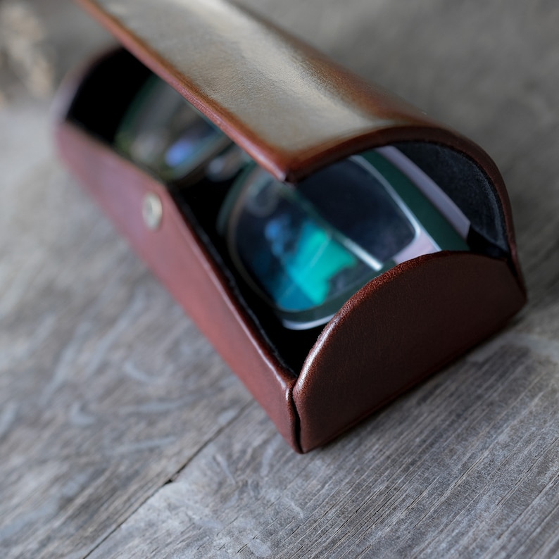 Pu&ograve; includere: Un astuccio per occhiali in pelle marrone con un paio di occhiali verde scuro e blu all'interno.