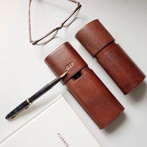 K&ouml;nnte beinhalten: Zwei braune Leder-Stift-Etuis, eines mit den Initialen "CJP" gepr&auml;gt auf der Oberseite. Ein F&uuml;llfederhalter liegt neben den Etuis.