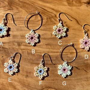 Puede incluir: Siete pares de pendientes de cuentas con un dise&ntilde;o de flor. Los pendientes est&aacute;n hechos con cuentas blancas, rosas y azul claro. Algunos pendientes tienen un dise&ntilde;o de aro, mientras que otros tienen un dise&ntilde;o de gota.