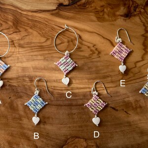 Puede incluir: Seis pares de pendientes con una variedad de colores y estilos. Cada pendiente presenta un peque&ntilde;o amuleto de forma cuadrada con una cuenta en forma de coraz&oacute;n que cuelga de &eacute;l. Los pendientes est&aacute;n etiquetados de la A a la F.