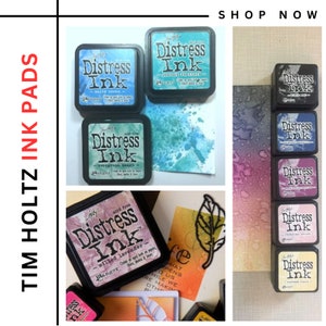Könnte beinhalten: Eine Sammlung von Tim Holtz Distress Ink Pads in verschiedenen Farben, darunter Salty Ocean, Evergreen Beach, Milled Lavender, Antique Linen und mehr. Die Ink Pads sind in einer Reihe auf einer weißen Oberfläche angeordnet. Der Text "Distress Ink" ist auf jedem Pad sichtbar.