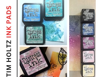 May include: A collection of Tim Holtz Distress Ink pads in various colors, including Salty Ocean, Evergreen Beach, Milled Lavender, Antique Linen, and more. The ink pads are arranged in a row on a white surface. The text "Distress Ink" is visible on each pad.