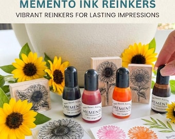 Puede incluir: La imagen presenta recargas de tinta Memento con sellos y flores de girasol. Los frascos de tinta son de varios colores, incluyendo verde oliva, rosa y naranja. El texto de la imagen dice "MEMENTO INK REINKERS" y "VIBRANT REINKERS FOR LASTING IMPRESSIONS."