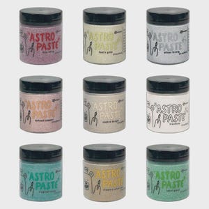 May include: Nine jars of Astro Paste with black lids and various colors. The jars are labeled with names like "bee sting," "fool's gold," and "silver lining." Each jar has a unique color and texture, with the text "ASTRO PASTE" prominently displayed.