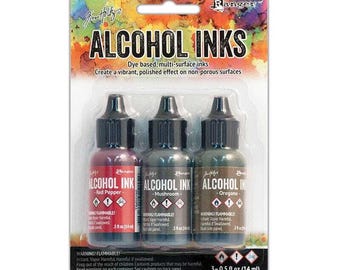 May include: A set of three 0.5 fl oz (14 ml) alcohol inks in red pepper, mushroom, and oregano colors. The inks are packaged in a clear plastic blister pack with a white background and black text. The text on the packaging reads "Ranger Alcohol Inks".