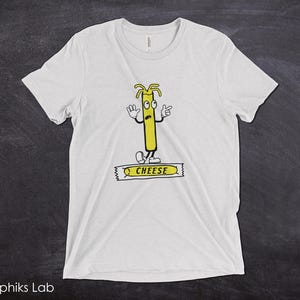 May include: White t-shirt with a cartoon illustration of a stick of cheese with a face and the word "CHEESE" printed on a yellow banner.