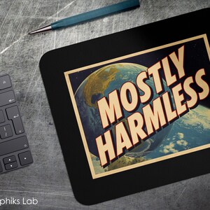 May include: Black rectangular mousepad with rounded corners featuring a retro-style image of Earth and the text "MOSTLY HARMLESS" in a bold, orange font. A black keyboard and a teal pen are also visible.