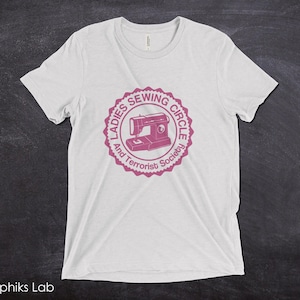May include: White t-shirt with a pink graphic of a sewing machine and the text "Ladies Sewing Circle and Terrorist Society".