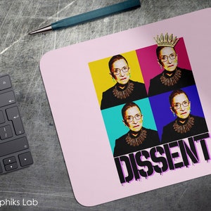 May include: Pink mouse pad with a pop art style image of Ruth Bader Ginsburg wearing a crown. The image is repeated four times in different colors. The text "DISSENT" is written in black with a pink outline.