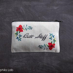 May include: A white canvas zippered pouch with a floral design and the text "Butt Stuff" in black cursive writing.