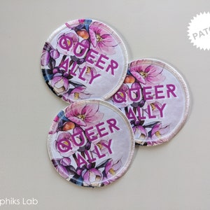 May include: Three round white fabric patches with pink floral designs and the text "Queer Ally" in pink lettering. The patches have a white border and are labeled "Patch" in the top right corner.