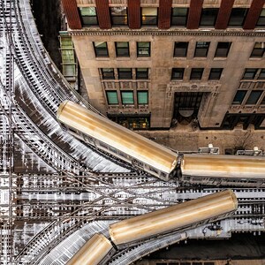 Pu&ograve; includere: Vista aerea di un incrocio di binari ferroviari in una citt&agrave;. I binari sono coperti di neve e ci sono quattro carrozze ferroviarie parcheggiate sui binari. Le carrozze ferroviarie sono di colore marrone chiaro e sono tutte rivolte nella stessa direzione. Le carrozze ferroviarie sono parcheggiate in una curva dei binari. I binari sono circondati da edifici.