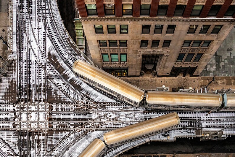 Pu&ograve; includere: Vista aerea di un incrocio di binari ferroviari in una citt&agrave;. I binari sono coperti di neve e ci sono quattro carrozze ferroviarie parcheggiate sui binari. Le carrozze ferroviarie sono di colore marrone chiaro e sono tutte rivolte nella stessa direzione. Le carrozze ferroviarie sono parcheggiate in una curva dei binari. I binari sono circondati da edifici.