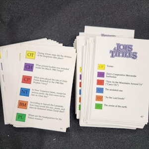 以下が含まれることがあります： 「Jots and Tittles」というタイトルのカラフルなカードの山で、旧約聖書、教会史、その他のトピックに関する質問と回答が書かれています。カードはゲームやクイズ用に設計されています。