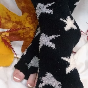Könnte beinhalten: Schwarze Zehensocken mit weißem Sternmuster. Die Socken sind aus einem weichen, flauschigen Material gefertigt. Das Bild zeigt auch ein gelbes und braunes Blatt.