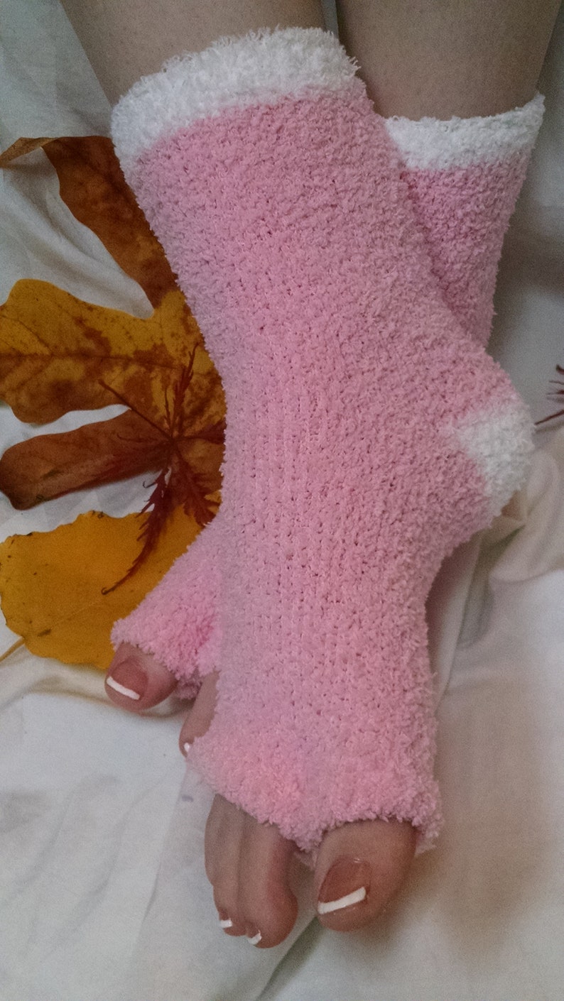 May include: A pair of pink fuzzy socks with white trim. The socks are worn on a person's feet and have white nail polish on the toes.