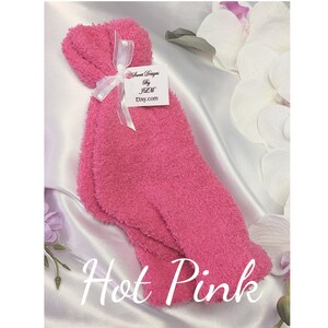 May include: A pair of fuzzy pink socks tied with a white ribbon and a tag that reads "Sweet Designs by JLM Etsy.com". The socks are on a white satin background. The text "Hot Pink" is written below the socks.