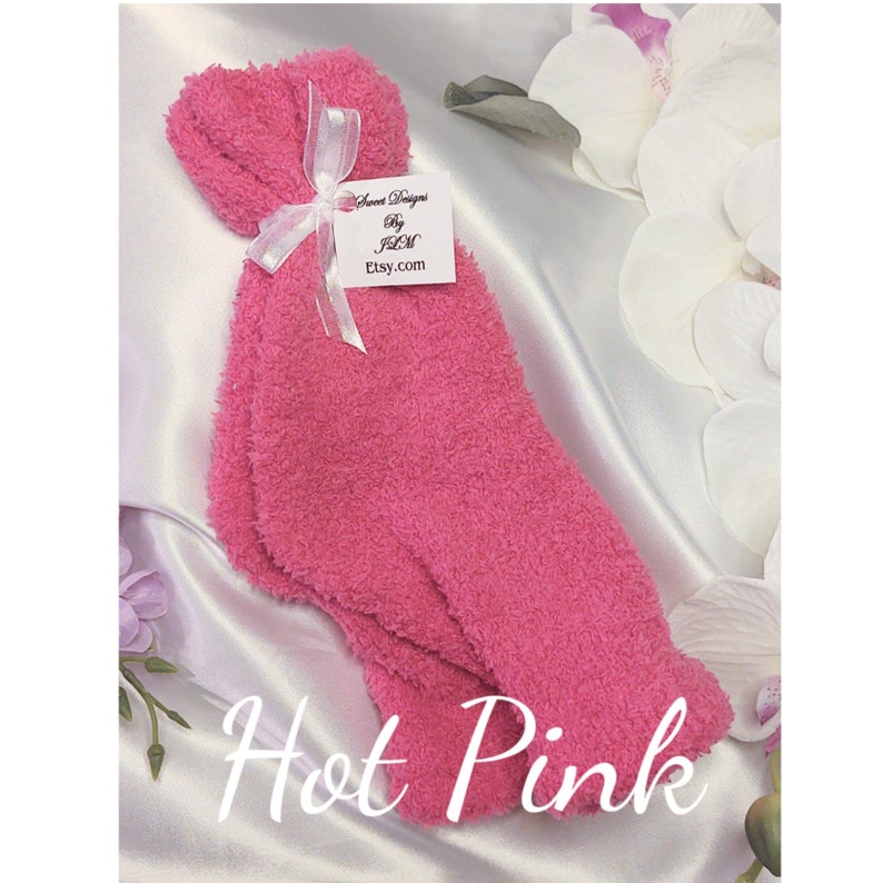 May include: A pair of fuzzy pink socks tied with a white ribbon and a tag that reads "Sweet Designs by JLM Etsy.com". The socks are on a white satin background. The text "Hot Pink" is written below the socks.