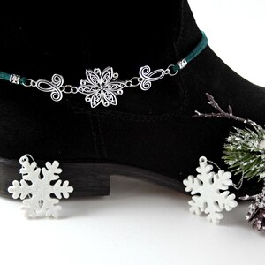 May include: A green suede ankle boot with a silver snowflake charm attached to the top of the boot. The charm is attached to a silver chain with a green cord.