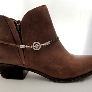 May include: Brown leather ankle boots with a silver and crystal ankle bracelet. The bracelet has a circular charm with a silver design.