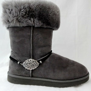 May include: Gray suede boots with a black cord and a silver decorative buckle. The boots have a faux fur cuff.