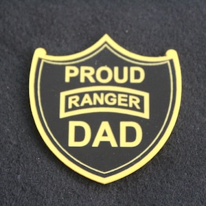 May include: Black and yellow shield-shaped patch with the text "Proud Ranger Dad" in yellow lettering.