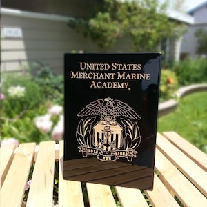 May include: Black plaque with gold lettering that reads "United States Merchant Marine Academy". The plaque features a gold eagle with a shield and anchor.