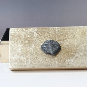 May include: A rectangular wooden box with a gold leaf finish on the lid. A dark gray stone is affixed to the top. The interior of the box is black. The box is open, revealing the interior.