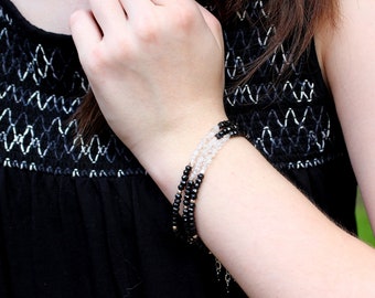 May include: A multi-strand bracelet featuring black and clear beads. The bracelet is worn on the wrist and has a delicate, layered design. The beads are strung together with a thin, metallic chain. The bracelet is a piece of jewelry.