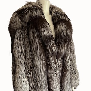 Puede incluir: Un abrigo de piel de zorro plateado de cuerpo entero con un cuello ancho. El abrigo se exhibe en un maniquí sobre un fondo blanco. El texto "find your dream fur at MOXIEFURS.COM" está en la parte inferior.
