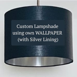 Puede incluir: Una pantalla de lámpara azul oscuro con interior plateado. La pantalla es cilíndrica y está suspendida de una varilla plateada. El texto en la pantalla dice "Custom Lampshade using own WALLPAPER (with Silver Lining)".