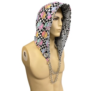 May include: A reversible hood with a chain necklace. One side features a black and white checkerboard pattern with pastel yin-yang symbols. The other side has a black and white swirling design. The hood is displayed on a mannequin.