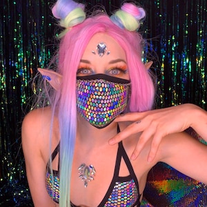 May include: A person wearing a black and iridescent face mask with a geometric pattern. The mask is made of sequins and has a black elastic band. The person is also wearing a black and iridescent bra with a geometric pattern. The bra has a black elastic band and a clasp in the back.