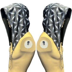 May include: A black hooded top with a white geometric pattern and gold chain accents. The top is displayed on a mannequin.