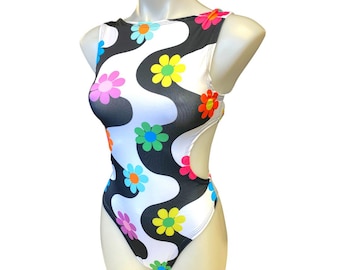May include: A white and black swimsuit with a colorful daisy print. The swimsuit has a scoop neck and a cutout on each side.