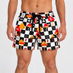 Può includere: Pantaloncini con motivo a scacchi bianco e nero con una stampa grafica ripetuta di funghi arancioni e rossi, occhi stilizzati e piccoli vortici neri. I pantaloncini includono una coulisse nera in vita con elastico.