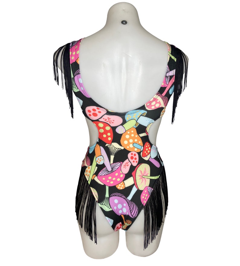 Puede incluir: Traje de ba&ntilde;o negro con estampado de setas de colores y ribete de flecos negros. El traje de ba&ntilde;o tiene recortes en los lados.