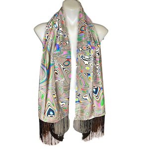 May include: A white scarf with a colorful abstract swirl pattern and black fringe. The scarf is made of a silky material and has a flowing drape.