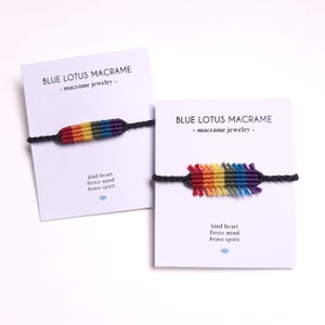 Puede incluir: Dos pulseras de amistad de colores arcoíris con cuerda negra. Las pulseras están en tarjetas blancas con el texto "BLUE LOTUS MACRAME - macramé joyería -" y "corazón amable mente feroz espíritu valiente".