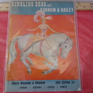 May include: A vintage circus magazine cover featuring a woman in a pink costume riding a white horse. The cover reads "Ringling Bros and Barnum & Bailey Circus Magazine & Program 1954 Edition 25c".