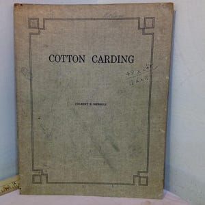 Op de afbeelding: Een oude boekomslag met de titel "COTTON CARDING" in zwarte hoofdletters. De omslag is een verbleekte bruinachtige kleur met een zwarte decoratieve rand. De naam van de auteur, Gilbert R. Merrill, is eronder gedrukt.
