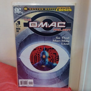 May include: A comic book cover featuring a blue and silver robot with a large eye in the center of its chest. The cover is titled "The OMAC Project" and has the text "...So That Man May Live" below the title. The cover also features the DC Comics logo and the text "6 Months Until Infinite Crisis".