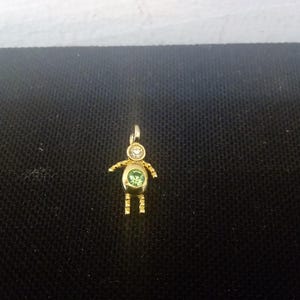 May include: A gold charm in the shape of a person with a green and white gemstone in the center.