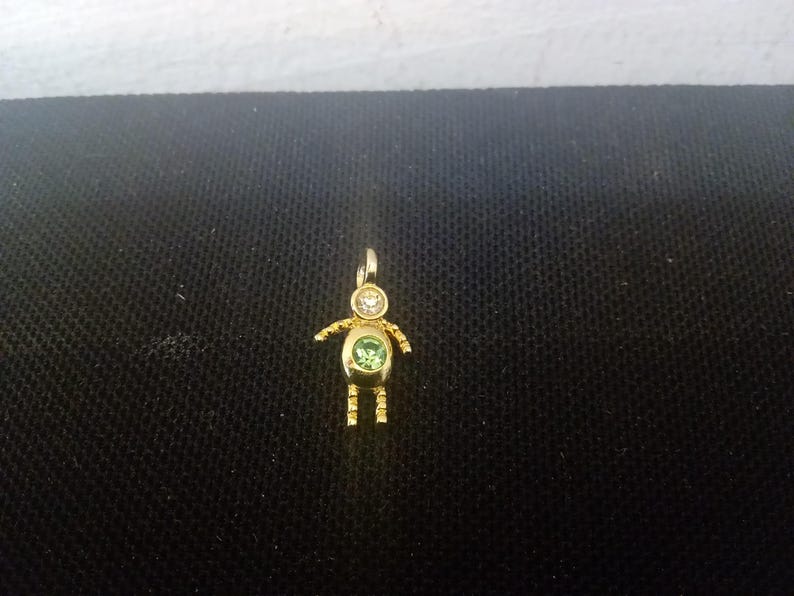 May include: A gold charm in the shape of a person with a green and white gemstone in the center.