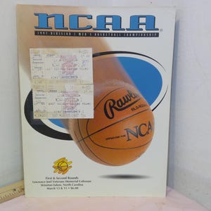 Op de afbeelding: Een vintage NCAA basketbalkampioenschapsprogramma-omslag met een basketbal en de tekst "NCAA 1997 Division I Men's Basketball Championship". Bevat een ticketstrookje en evenementdetails.