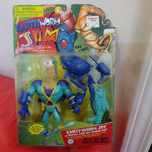 May include: Earthworm Jim action figure in a sealed package. The figure is a teal and purple worm-like character with a clear helmet. The packaging features the Earthworm Jim logo and the text "In Special Deep Sea Mission Suit".