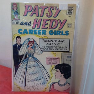 Può includere: Copertina di fumetto vintage "Patsy and Hedy Career Girls" con una sposa in abito da sposa e la scritta "Marry Me, Patsy!". L'illustrazione è in rosa, blu e bianco.